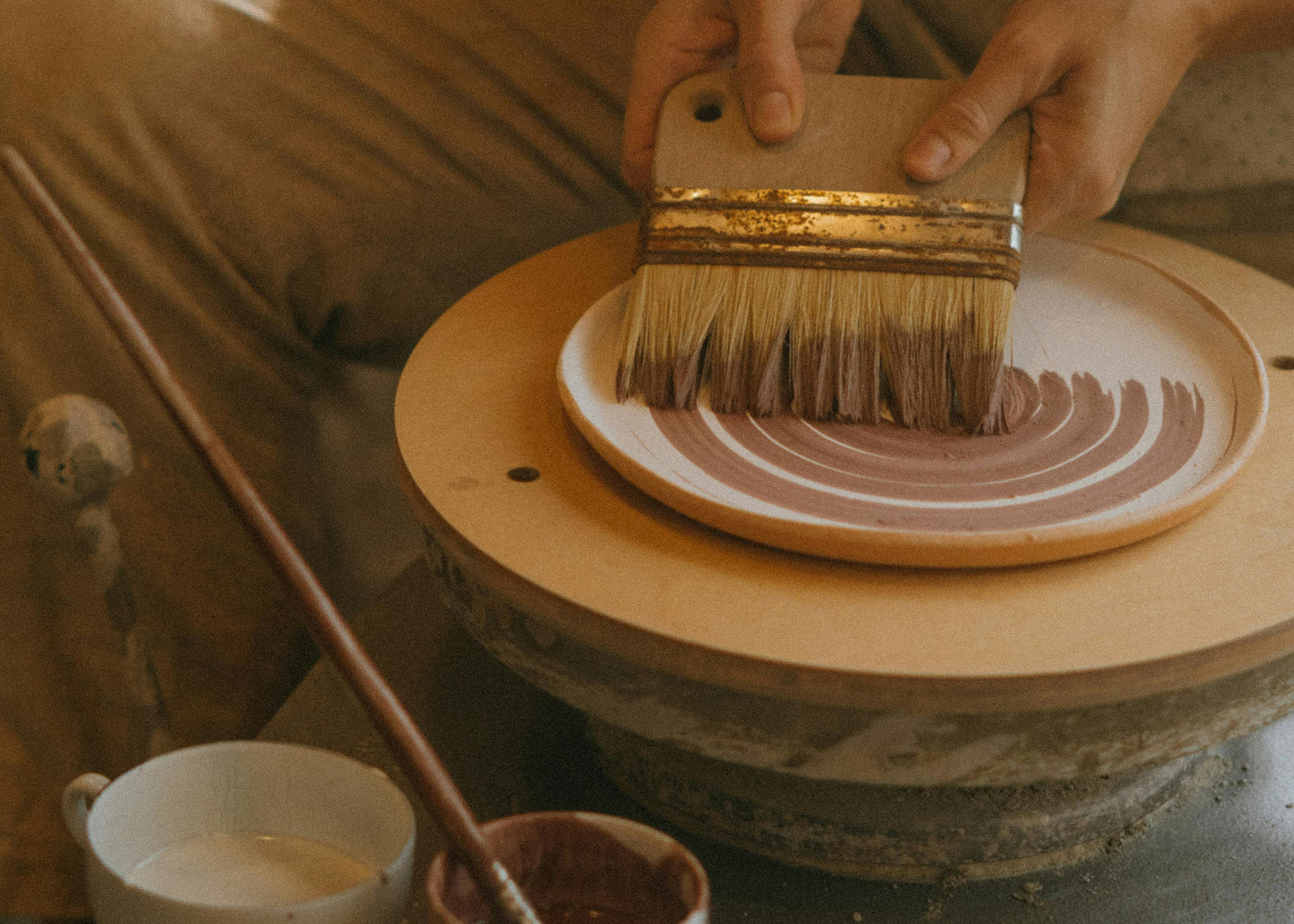 Person working with pottery, applying glaze to a ceramic piece on a banding wheel.
