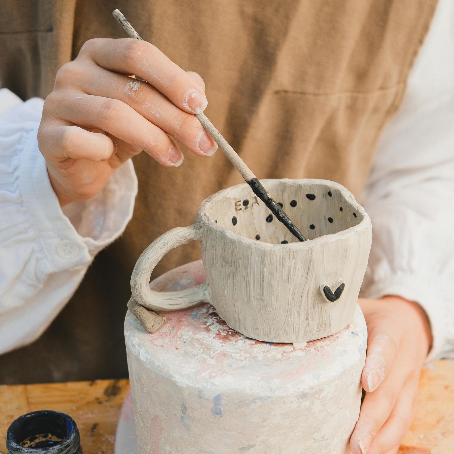 Person decorating a clay mug with a small heart design and dots