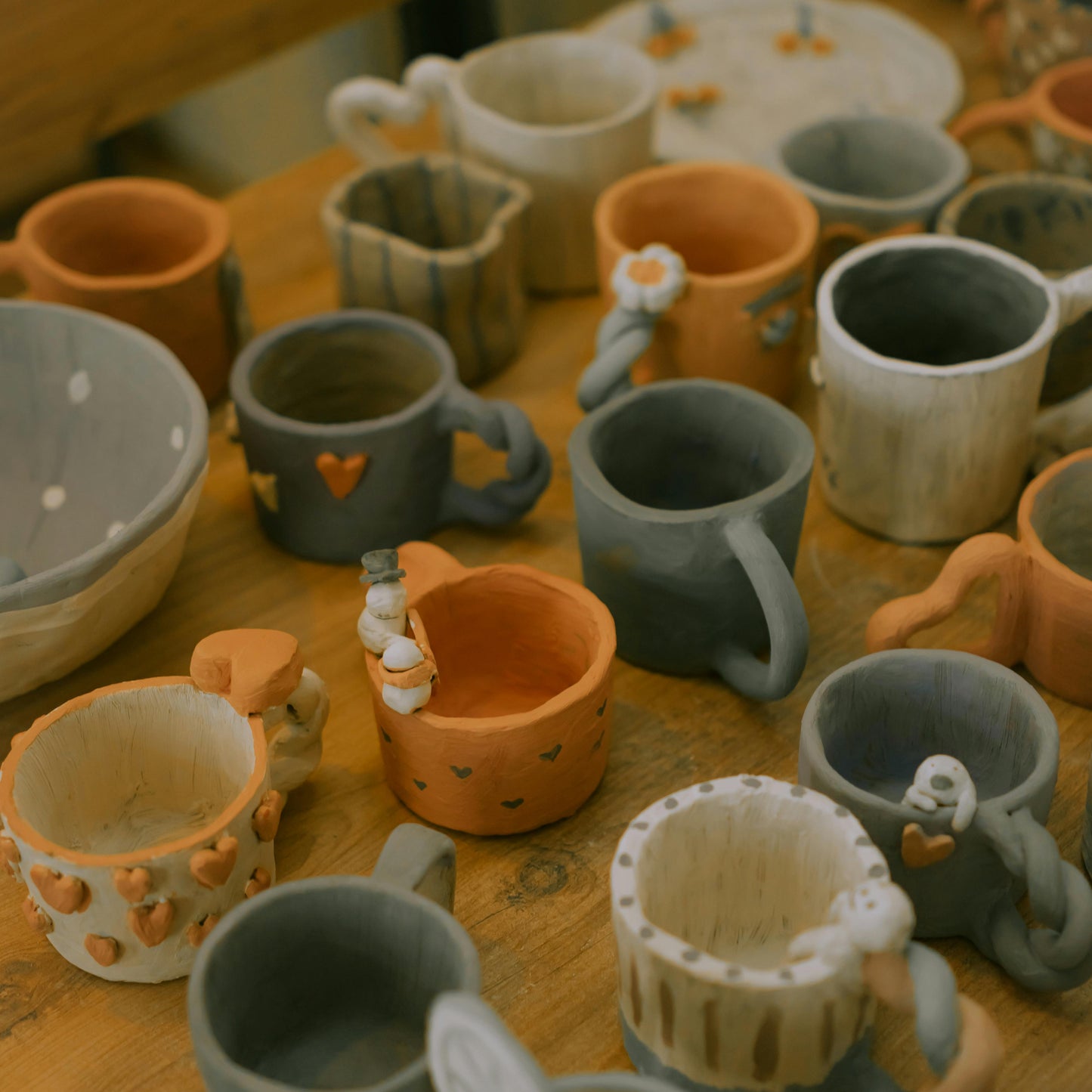 Assorted handmade mugs with cute hearts, flowers and creatures decorating their handles, rims or sides