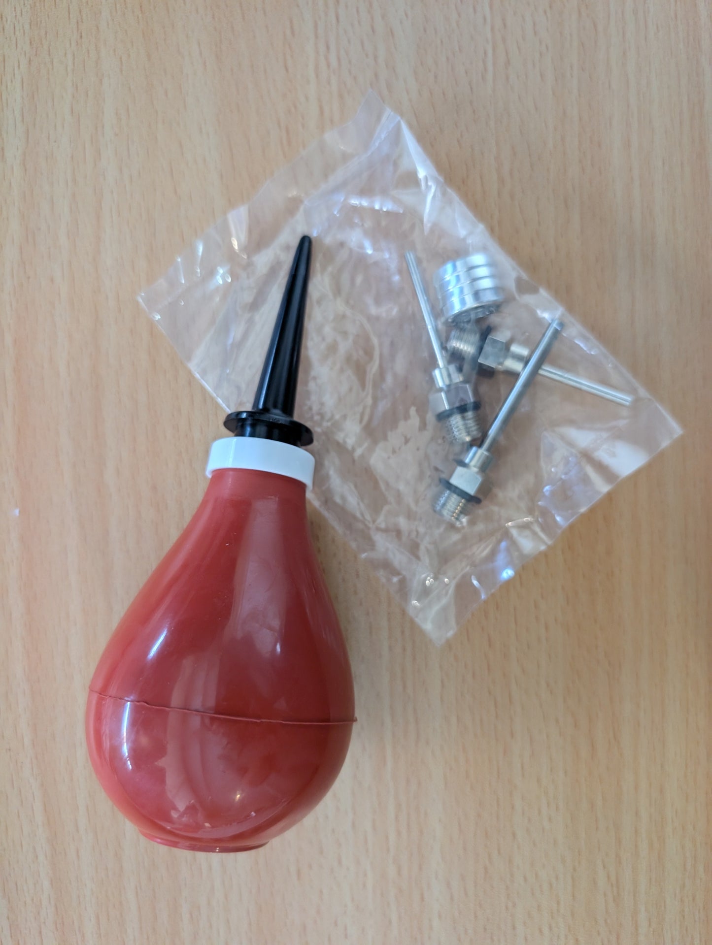Red bulb shaped syringe-like device with interchangeable nozzles on a wooden surface