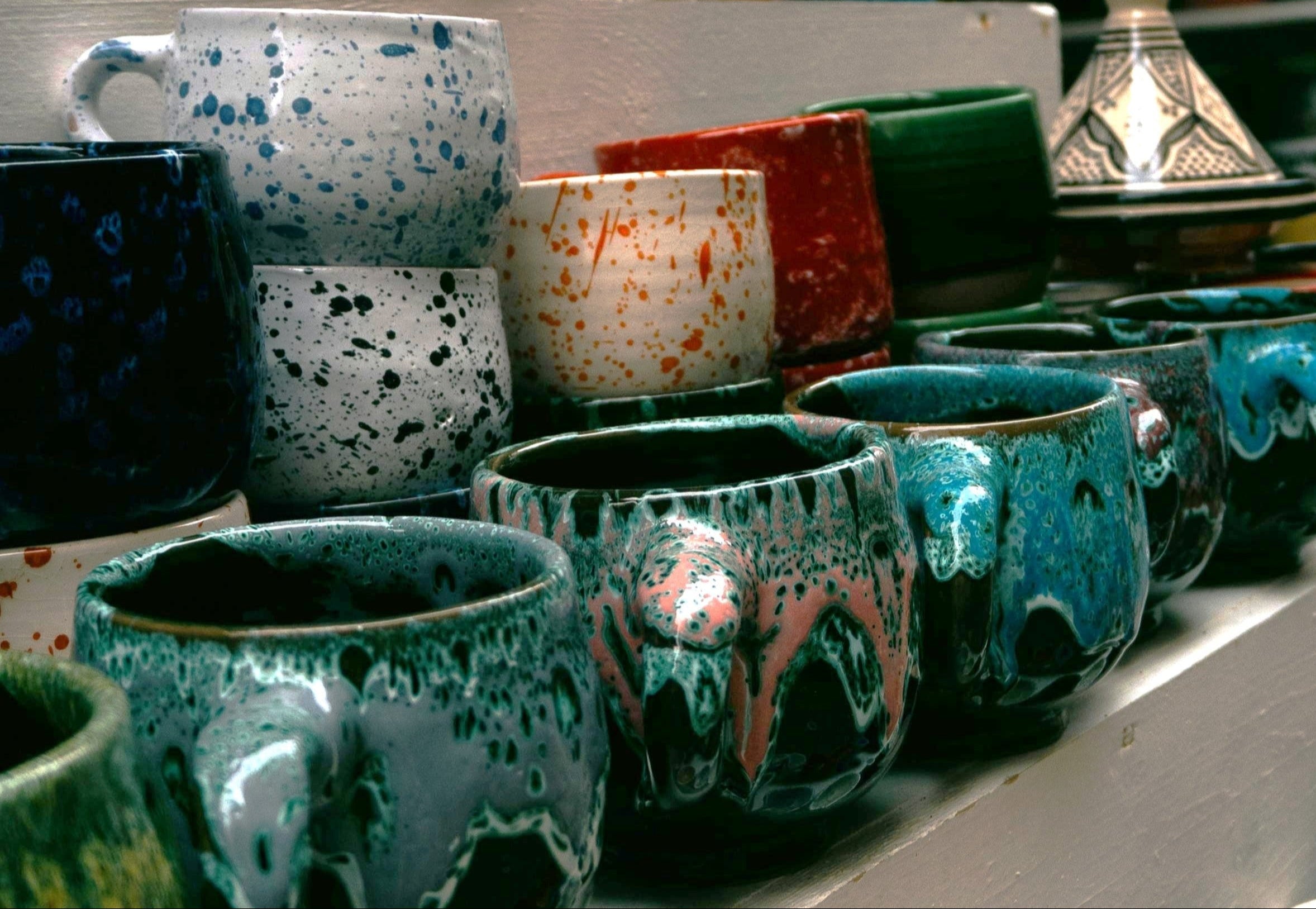 Colourful mugs on a shelf featuring multi-coloured glazes with spatter or drippy effects