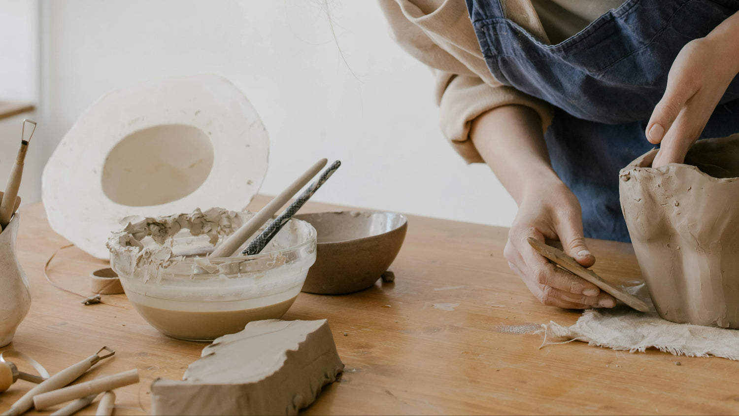 Person sculpting a clay vessel in a pottery studio