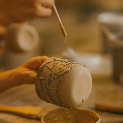 Person decorating a clay cup with drizzles of slip or glaze
